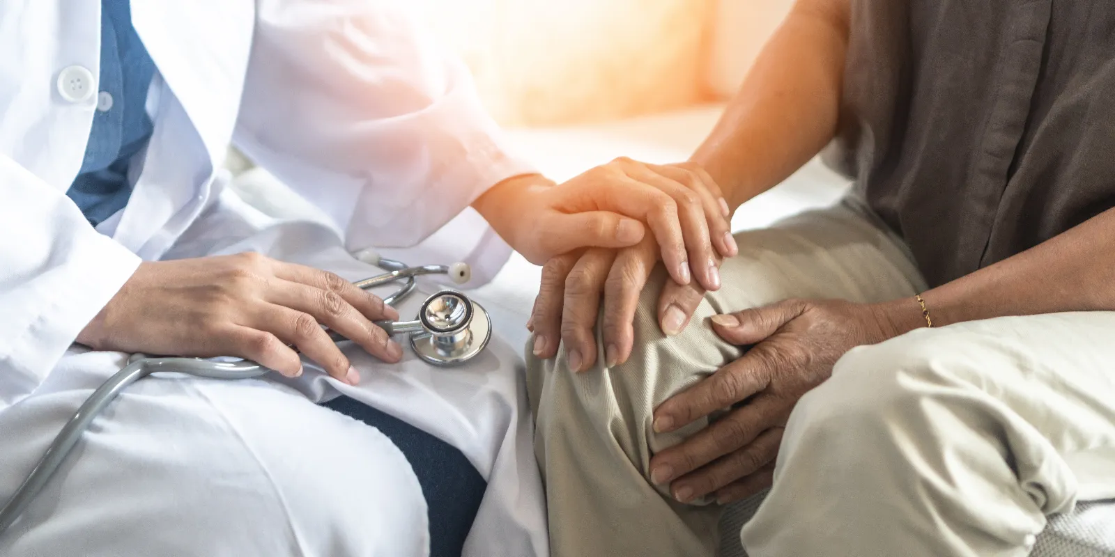 Läkare håller en äldre patients hand.